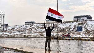 Un homme arbore un drapeau syrien en contrebas d’un convoi d’évacuation d’Alep Est transportant des combattants rebelles ou des civils. © Reporters / Photoshot