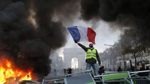 Tel Marianne sur les barricades, un Gilet jaune brandit le drapeau français. À Paris, la manifestation sur les Champs-Elysées, samedi, a  tourné à l’émeute.