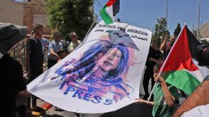 Des activistes palestiniens et israéliens soulèvent des drapeaux palestiniens et une banderole représentant la journaliste américano-palestinienne Shireen Abu Akleh, à Jérusalem-Est, pendant la visite du président américain, le 15 juillet 2022, pour lui demander de dénoncer sa mort.