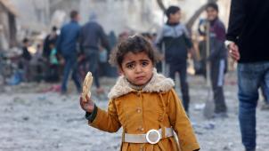 Une fille palestinienne mange un morceau de pain alors que les gens vérifient les dégâts après des frappes aériennes israéliennes dans le camp de réfugiés de Rafah.