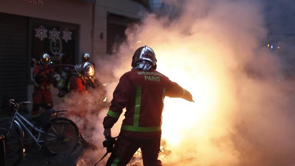 Des pompiers français tentent d’éteindre une voiture en feu lors des débordements de la manifestation des « gilets jaunes » samedi à Paris. La foule manifestait contre le président Emmanuel Macron et les taxes jugées trop hautes.