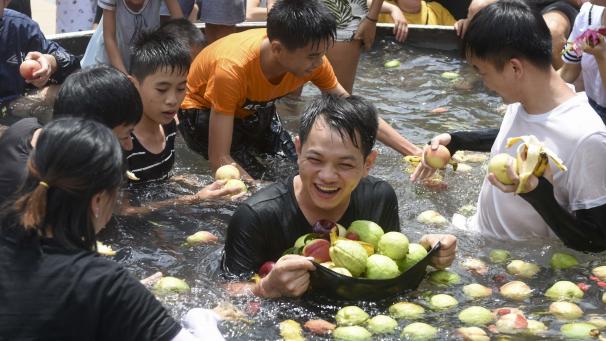 Des touristes mangent des fruits dans un seau de glace géant pour se rafraîchir lors d’une chaude journée dans une attraction en Chine.