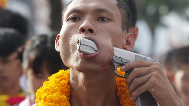 Pendant le festival annuel végétarien, à Phuket, un homme pointe une arme à travers sa joue percée.
