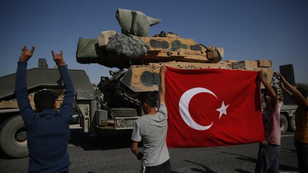 Les résidents locaux applaudissent alors qu’un convoi de camions des forces turques transportant des chars est conduit dans la province de Sanliurfa, dans le sud-est de la Turquie, à la frontière avec la Syrie.