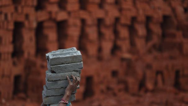 Une femme indienne, migrante, porte des briques sur sa tête au Népal.