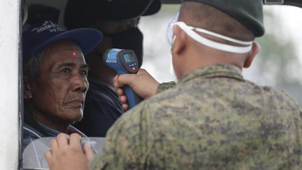 La température d’un homme est vérifiée par un soldat avant d’entrer dans la métropole à un point de contrôle à la périphérie de la ville de Quezon, aux Philippines.