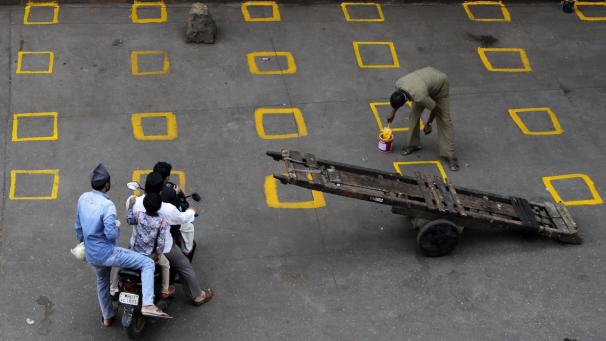 Des travailleurs tracent des marques au sol pour délimiter et maintenir la distance physique sur un marché à Mumbai, en Inde.