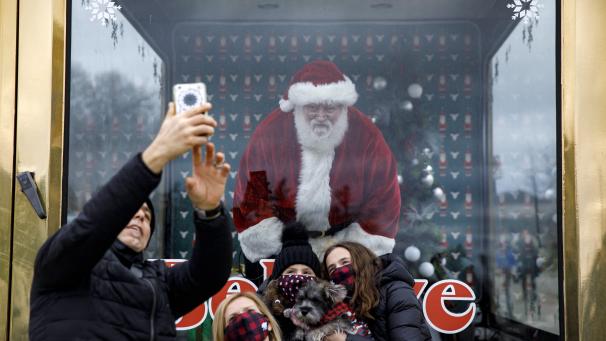 Un homme déguisé en père Noël prend des photos avec des familles derrière une paroi vitrée à Vaughan, au Canada.