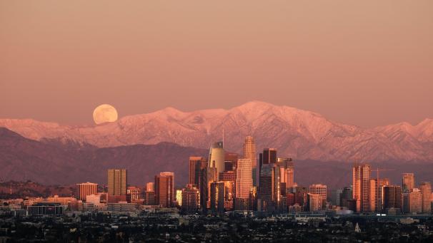 La lune se lève sur des montagnes couvertes de neige, derrière le centre-ville de Los Angeles.