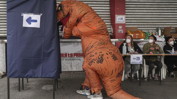 Une personne déguisée en dinosaure va voter au Chili.