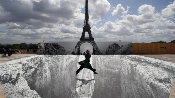 Une femme saute sur la place du Trocadéro devant la Tour Eiffel où l’artiste et photographe français connu sous le nom de JR expose son œuvre, à Paris.