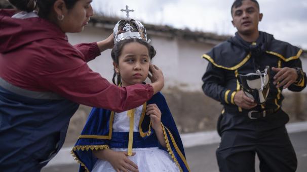 Une femme place une couronne sur la tête de sa fille âgée de 7 ans et habillée en Vierge de l
