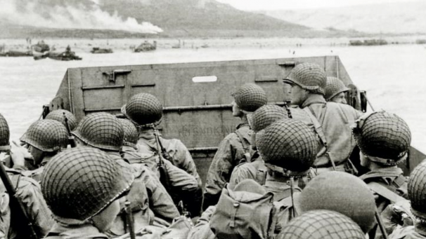 Des soldats américains aperçoivent la Normandie depuis leur bateau, avant de débarquer sur Omaha Beach. De loin, on peut apercevoir des véhicules déjà sur place et de la fumée.