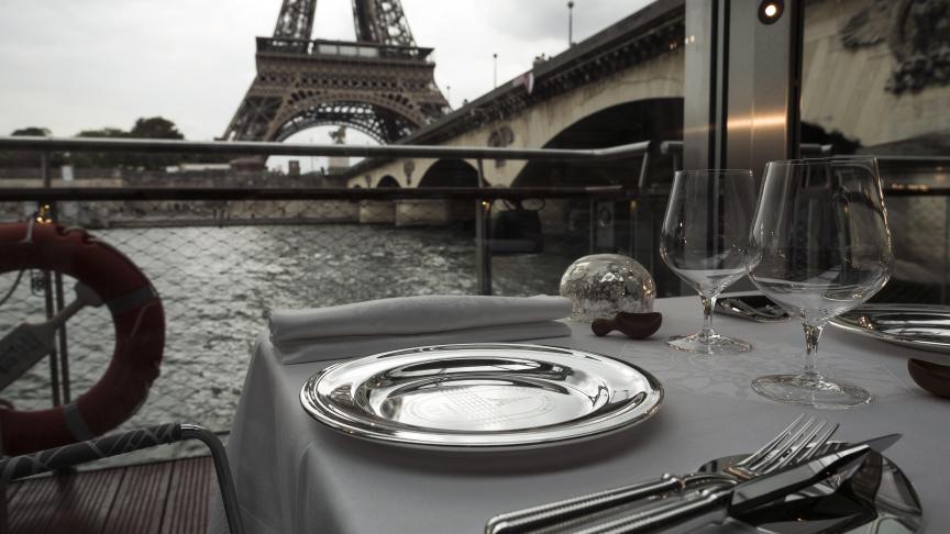 A dressed table is seen at French chef Alain Ducasse's new boat restaurant, the Ducasse sur Seine, on August 30, 2018 in Paris, next to the Eiffel tower (C). - Still smarting from being kicked out of his Michelin-starred restaurant halfway up the Eiffel Tower, France's most famous chef Alain Ducasse is pressing on instead with a new restaurant almost directly underneath it -- and, he boasts, it floats. Ducasse, who has won a total 21 Michelin stars -- more than any other chef alive -- will be dishing up lobster and duck foie gras onboard an electric boat on the River Seine from September 10. (Photo by Lionel BONAVENTURE / AFP)