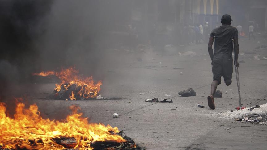 Un manifestant en béquilles passe devant des pneus en feu lors d’une manifestation pour demander la démission du Président Jovenel Moise, à Port-au-Prince (Haïti).