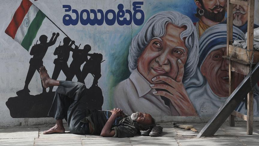 En Inde, un sans-abri se repose au sol devant des portraits de Mère Teresa et de l’ancien président A.P.J. Abdul Kalam.