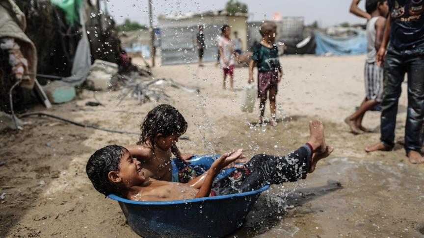 Des enfants palestiniens jouent avec de l’eau dans un bidonville à la périphérie du camp de réfugiés de Khan Yunis, dans le sud de la bande de Gaza, pendant une vague de chaleur.