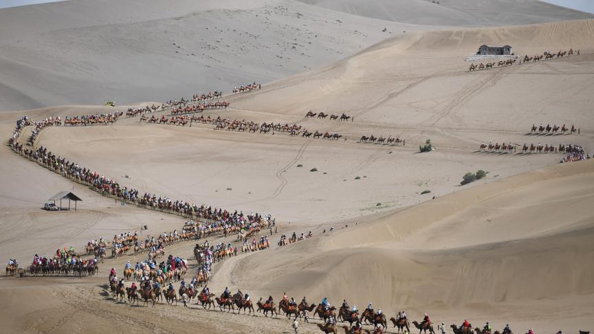 Des touristes chevauchent des chameaux à Mingsha Mountain et à Crescent Lake à Dunhuang, dans la province de Gansu, en Chine.