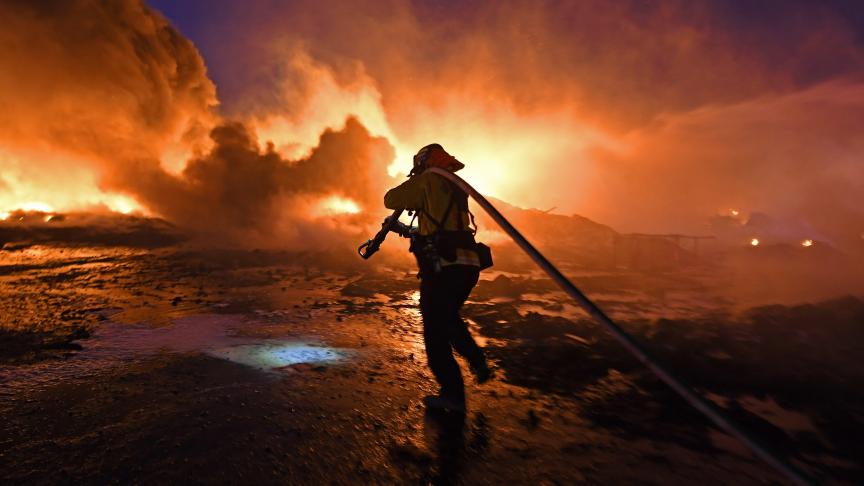 Un pompier tire un tuyau d’arrosage pour combattre un violent incendie d’herbe sur East Cypress Road à Knightsen en Californie.