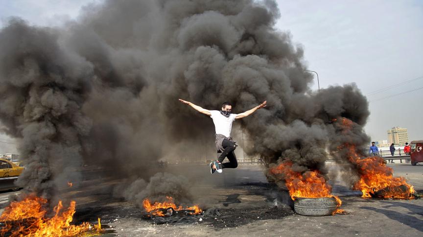 Un manifestant anti-gouvernement saute sur des pneus en feu bloquant une autoroute à Bagdad, en Irak.
