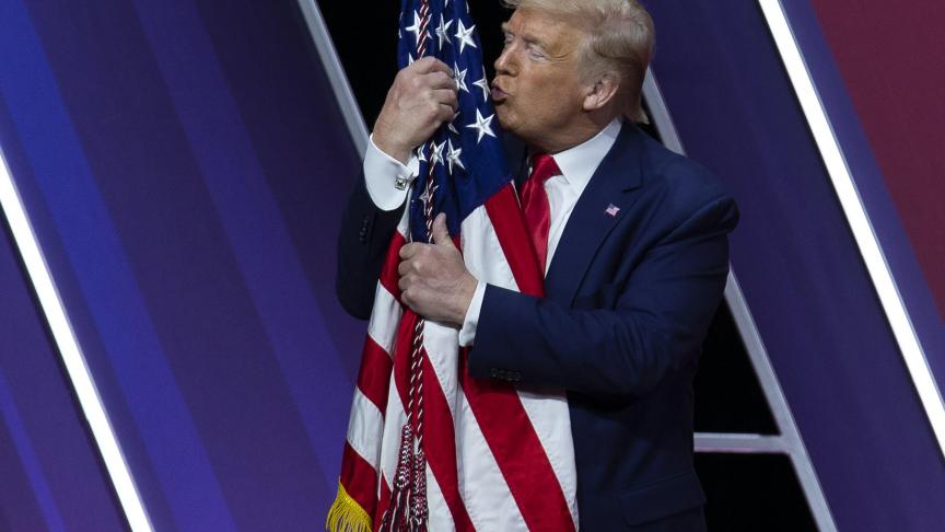 Le président Donald Trump embrasse le drapeau américain après avoir pris la parole à la Conférence d’action politique conservatrice, à Oxon Hill aux Etats-Unis.