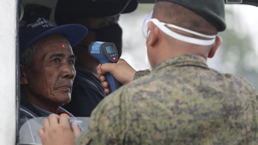 La température d’un homme est vérifiée par un soldat avant d’entrer dans la métropole à un point de contrôle à la périphérie de la ville de Quezon, aux Philippines.