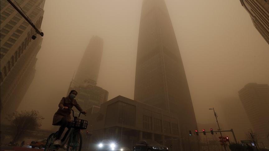 Un cycliste et des automobilistes passent devant des immeubles de bureaux au milieu d’une tempête de sable à l’heure de pointe dans le quartier central des affaires de Beijing.