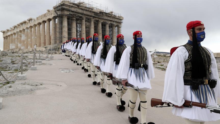 Des membres de la Garde présidentielle marchent devant le temple du Parthénon au sommet de la colline de l’Acropole après la cérémonie de levée du drapeau grec à Athènes.