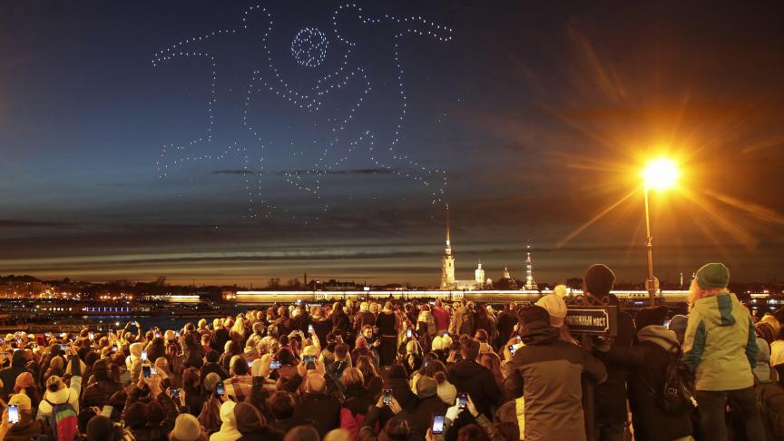 Des personnes observent des drones représenter des joueurs de foot dans le ciel à Saint-Pétersbourg en Russie.