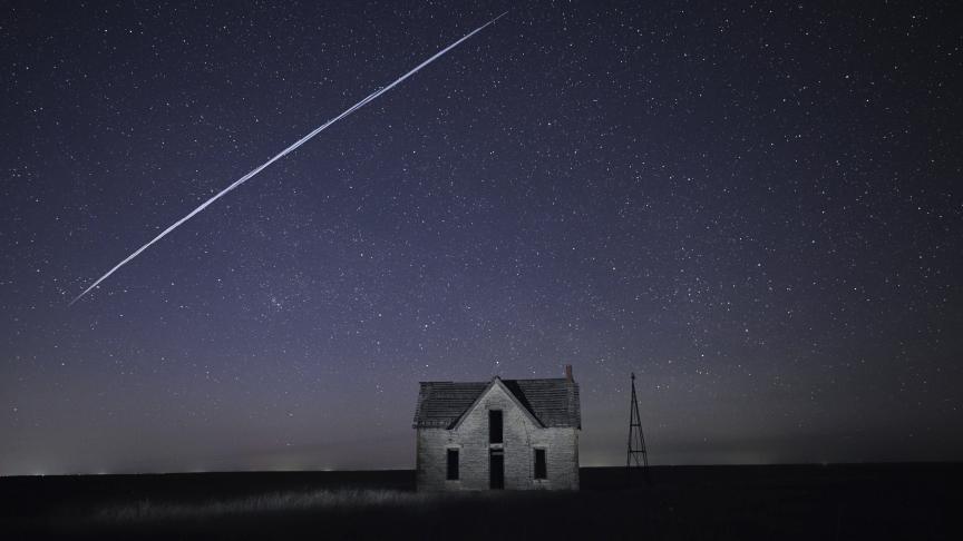 Sur cette photo prise avec une longue exposition, on aperçoit une série de satellites SpaceX StarLink passer au-dessus d’une vieille maison de pierres près de Florence.
