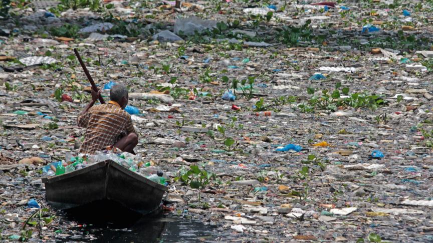 Un habitant du village de Sadar Ghat au Bangladesh se déplace en bateau tout en recueillant des bouteilles en plastique sur le fleuve Burigangan, particulièrement pollué.