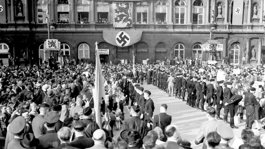 Le 2 septembre 1941, devant la gare du Nord, sur la place Rogier à Bruxelles, encadrées par les miliciens de DeVlag, des familles belges attendent leurs enfants qui ont passé leurs vacances en Allemagne.