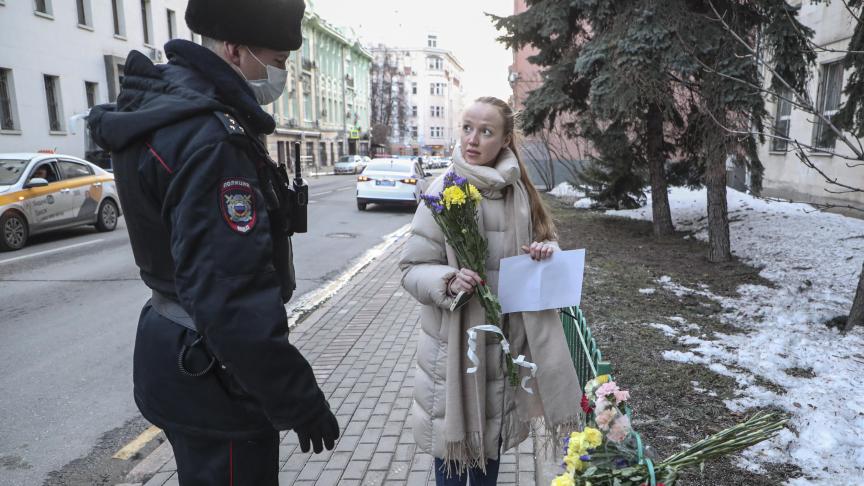 Une femme dépose des fleurs devant l'ambassade d'Ukraine dans le centre de Moscou. Un officiel russe veille.
