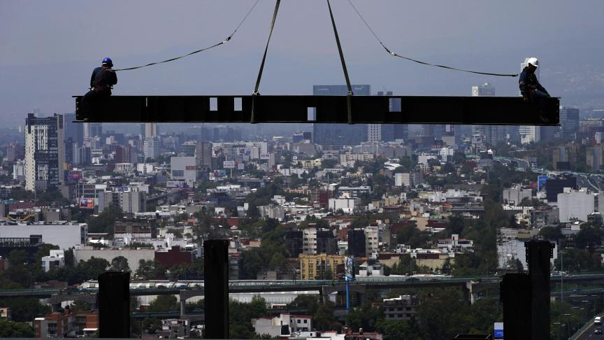 Des ouvriers du bâtiment montent sur une poutre suspendue à une grue sur le chantier de construction d'un immeuble résidentiel de grande hauteur à Mexico.