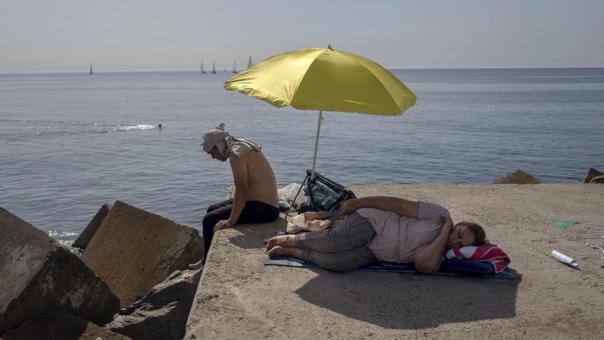 Une femme dort sous un parapluie sur un brise-lames devant la mer Méditerranée à Barcelone, en Espagne.
