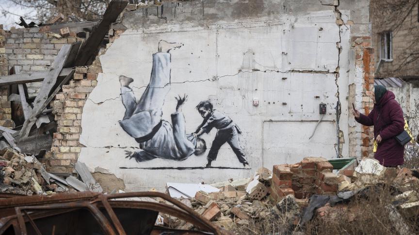 Une femme prend une photo d'une œuvre de Banksy sur un bâtiment détruit par les combats à Borodyanka, dans la région de Kyiv, en Ukraine.