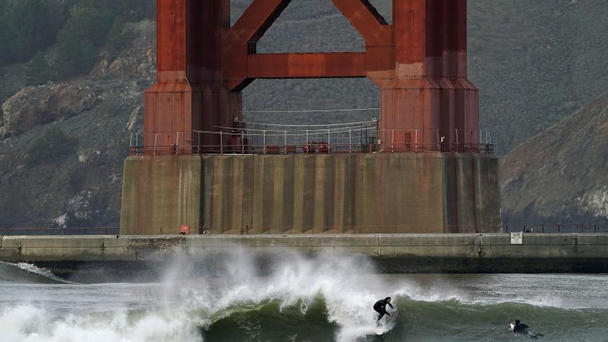 Les surfeurs se retrouvent sur les vagues devant une tour du Golden Gate Bridge à Fort Point à San Francisco.