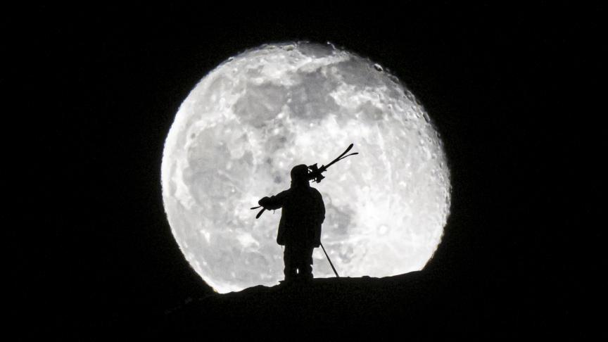 Un homme porte ses skis pendant le lever de lune au-dessus de la station alpine de Gryon, en Suisse, le mardi 7 février 2023.