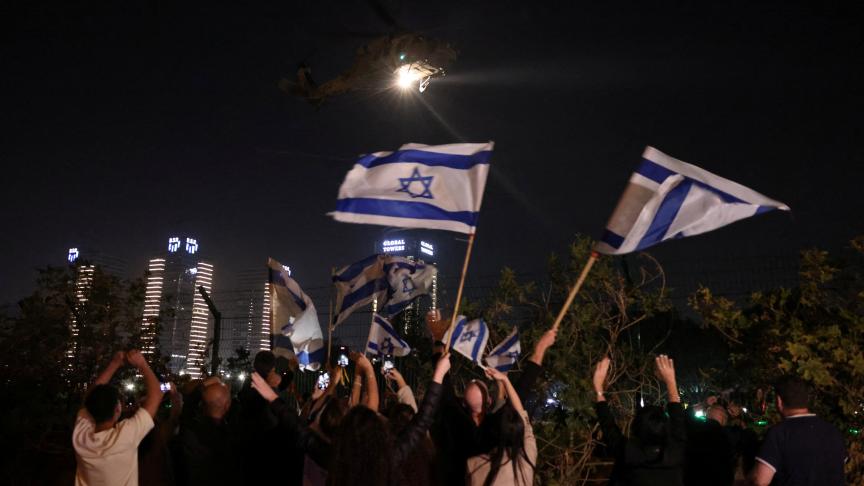 Des personnes agitent des drapeaux israéliens alors qu’un hélicoptère transportant des otages libérés dans le cadre d’un accord entre Israël et le groupe islamiste palestinien Hamas arrive au centre médical pour enfants Schneider à Petah Tikva, Israël, 24 novembre 2023. 