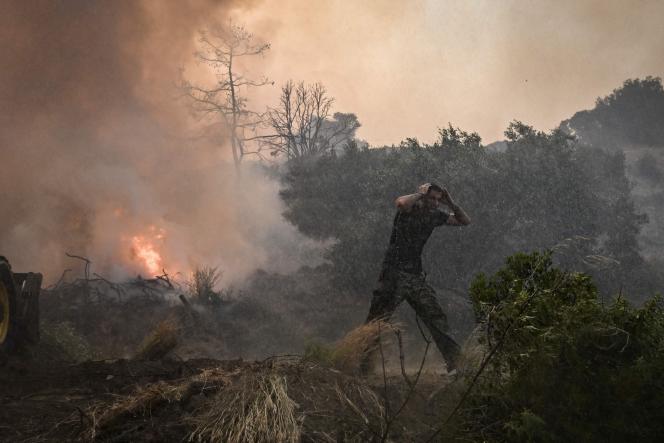 Un homme réagit alors qu’un hélicoptère pulvérise de l’eau sur un incendie à Gennadi, dans la partie sud de l’île grecque de Rhodes, le 25 juillet 2023, le 25 juillet 2023, lors d’un incendie de forêt.